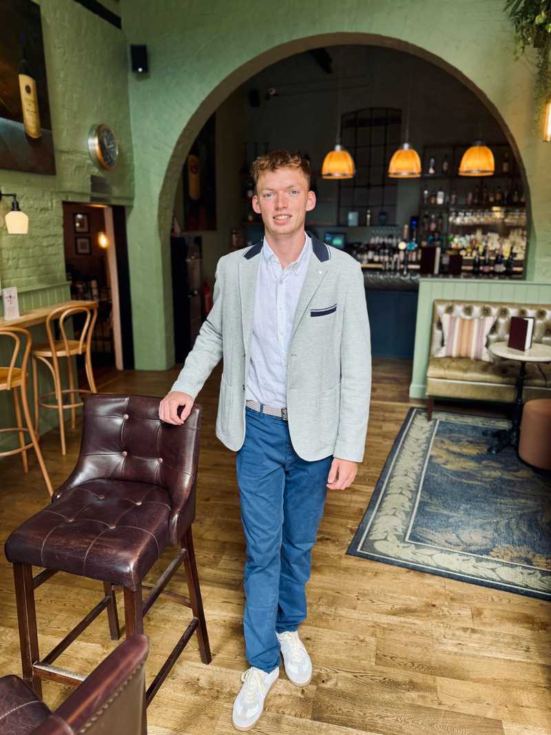 Filip Walter v saku stojí u barové židle v restauraci se zelenými stěnami